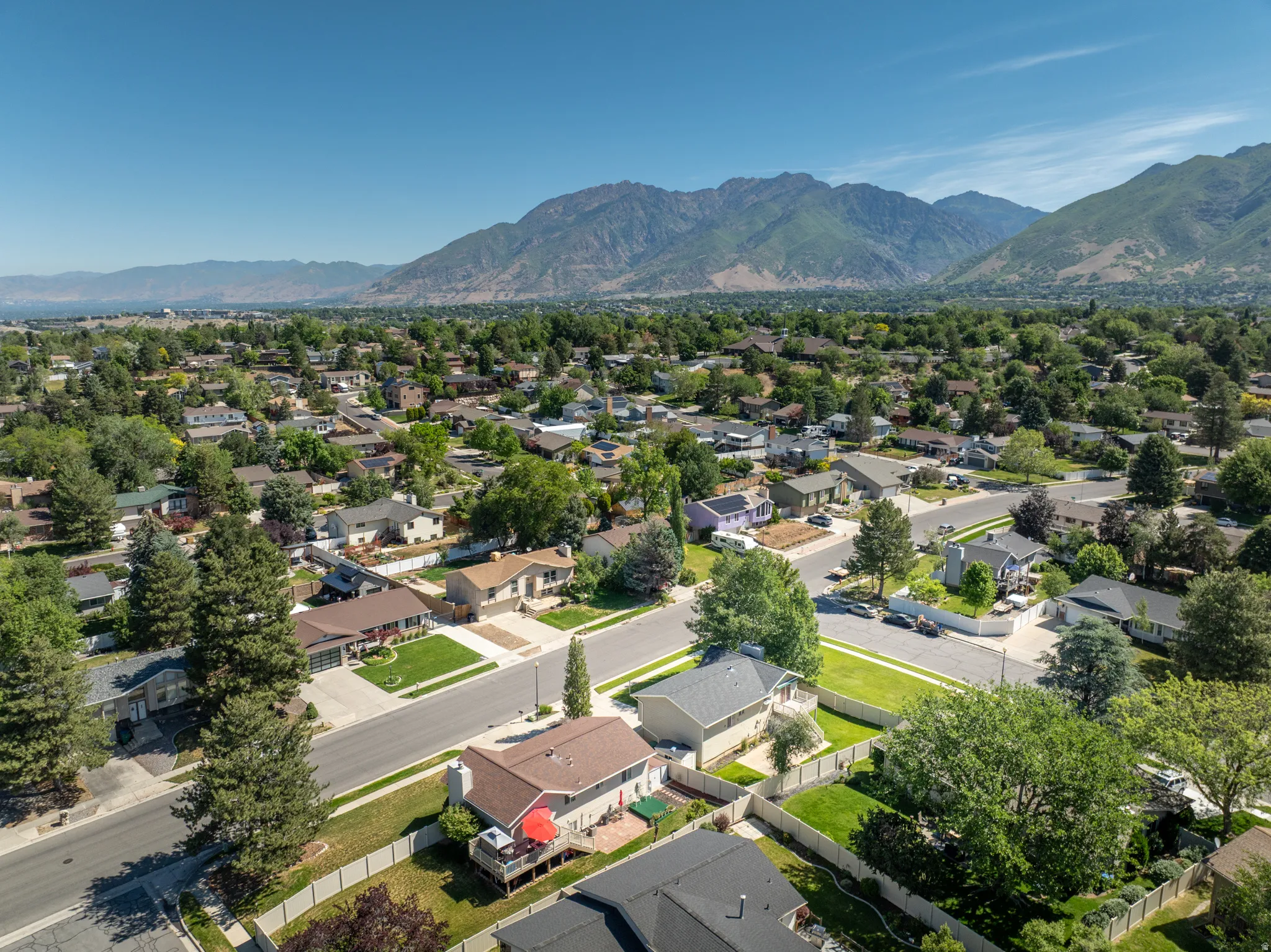 Expansive residential neighborhood featuring numerous single-family homes, mature trees, and paved streets, all set against a prominent mountain range backdrop