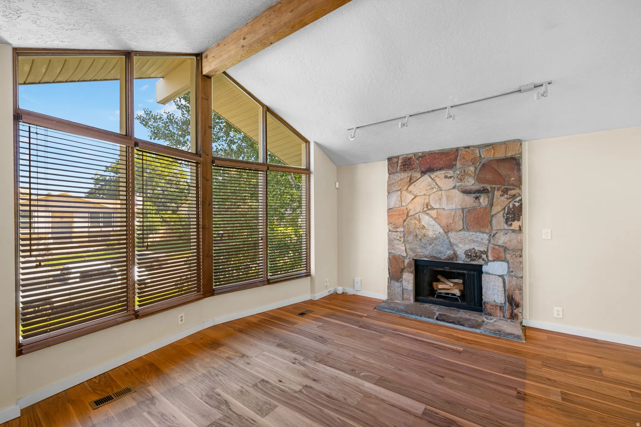 Vaulted ceiling with exposed wood beam, a stone-clad fireplace, and track lighting