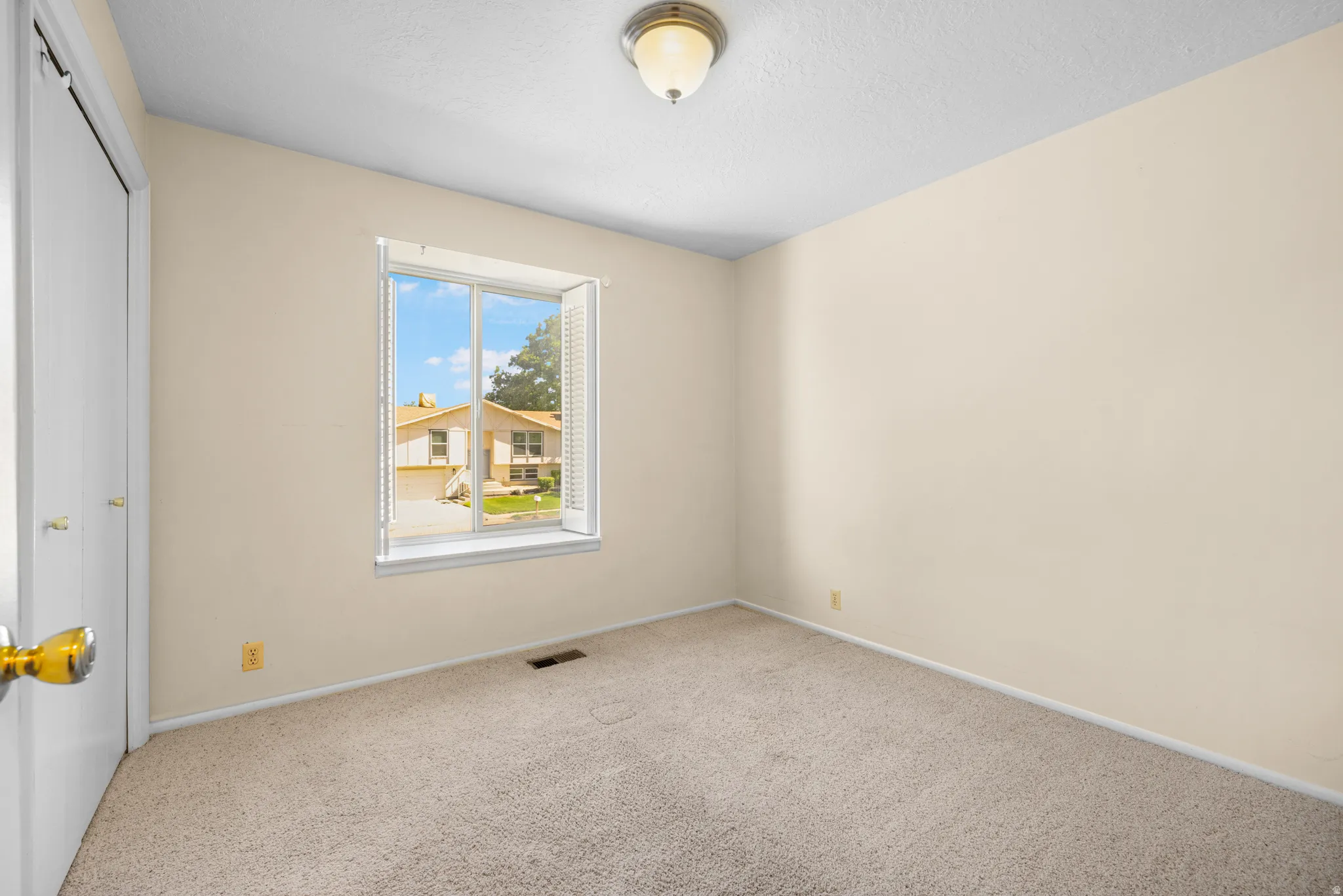 Carpeted interior space featuring a window with white louvered blinds, light-colored walls, a ceiling-mounted light fixture, and a white bi-fold closet door