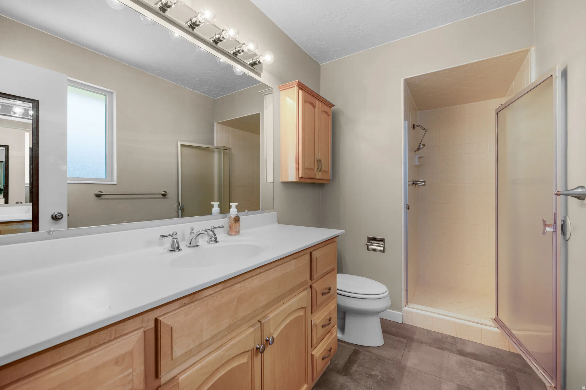 Bathroom featuring a single-basin vanity with wood cabinetry and a light-toned countertop, a frameless mirror, and a shower enclosure with a frosted glass door