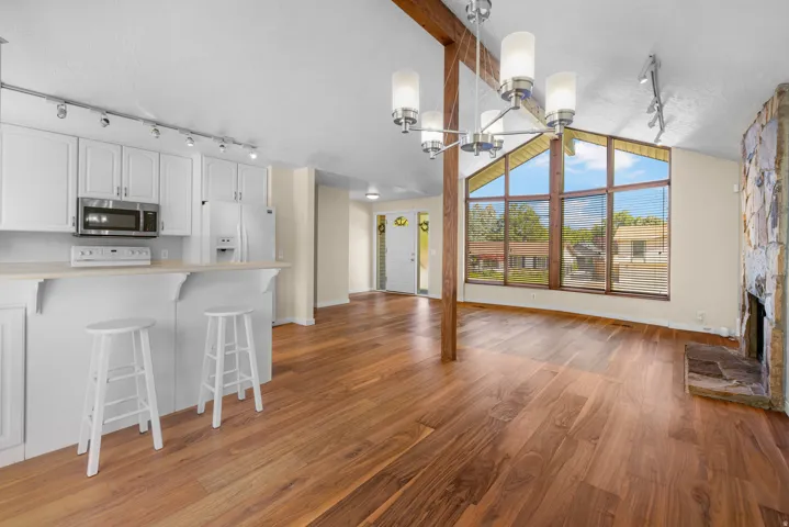 Open-concept living space featuring wood-finish flooring, a stone fireplace, and a large picture window
