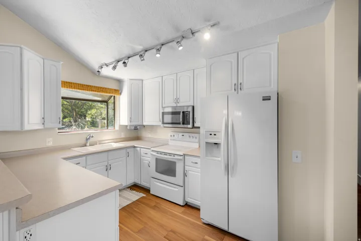 Kitchen featuring white cabinetry, light countertops, wood-finish flooring, and a vaulted ceiling