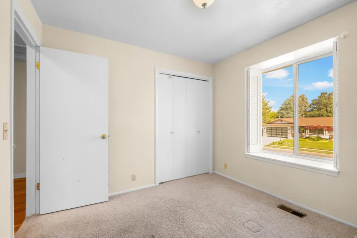 Carpeted room featuring a double window with exterior street scenery, bi-fold closet doors, and an overhead light fixture