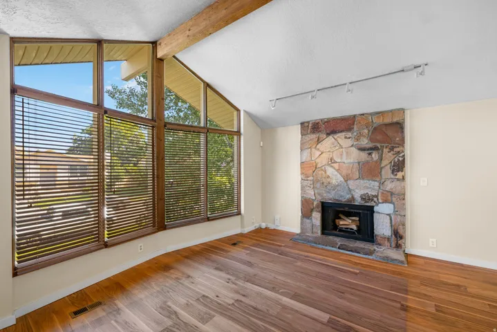Vaulted ceiling with exposed wood beam, a stone-clad fireplace, and track lighting