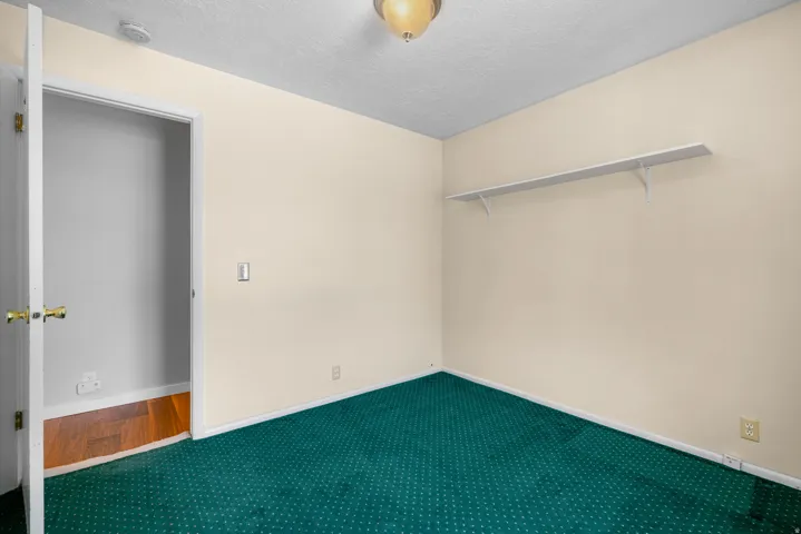 Room with green patterned carpeting, light beige walls, and white baseboards