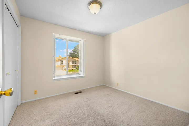 Carpeted interior space featuring a window with white louvered blinds, light-colored walls, a ceiling-mounted light fixture, and a white bi-fold closet door