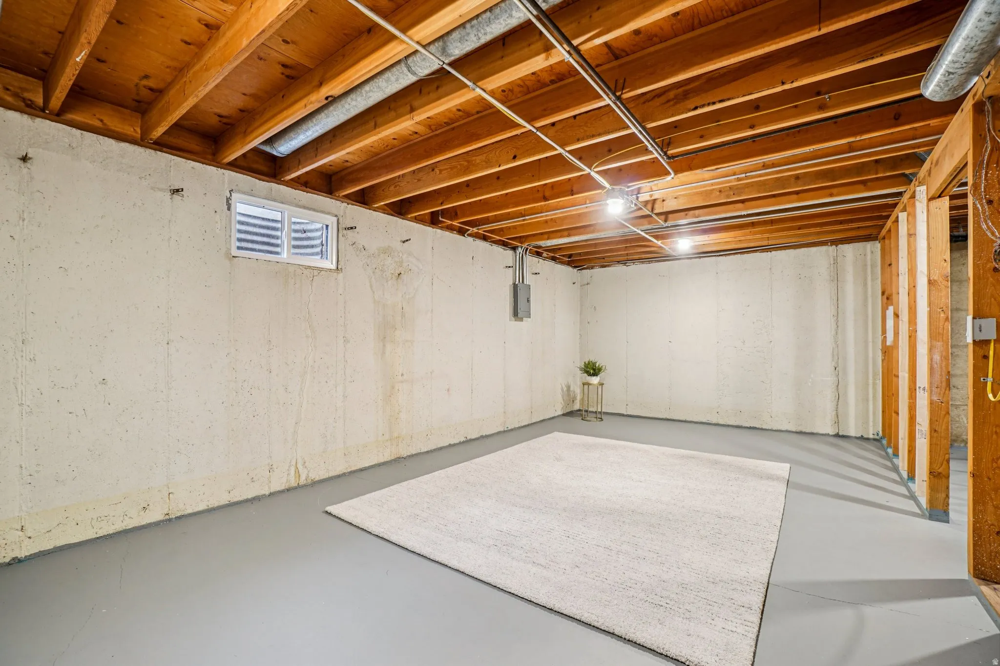 Unfinished lower level featuring exposed wood ceiling joists and painted concrete flooring