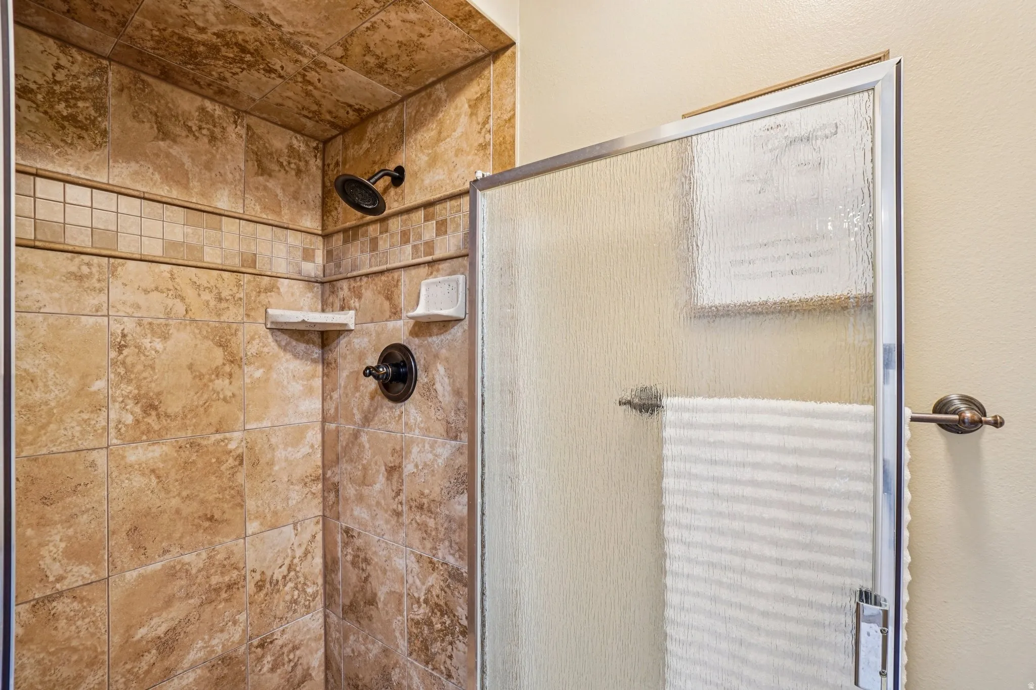 Tiled shower with a decorative mosaic band, bronze-finish fixtures, and a textured glass enclosure