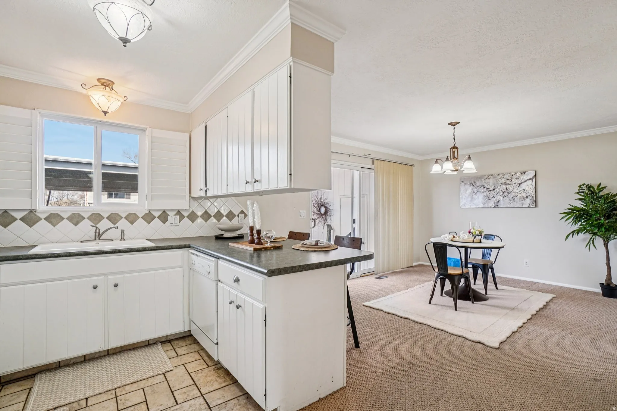 Bright kitchen featuring white cabinetry, a tiled backsplash with diamond accents, and dark countertops