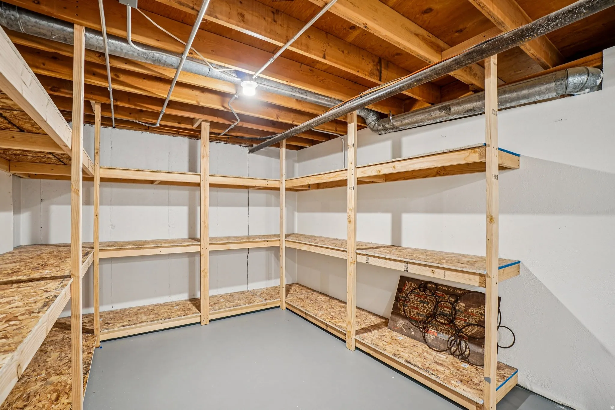 Basement storage area featuring extensive built-in shelving, painted concrete flooring, and exposed ceiling joists