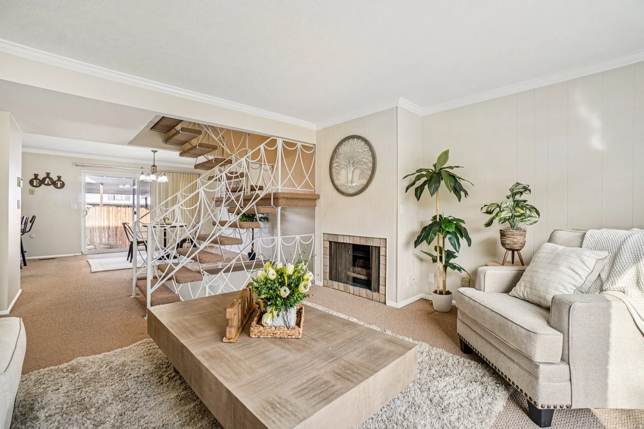 Open concept living area featuring a prominent staircase with decorative metal railing, a brick-surround fireplace, and light-toned wall paneling