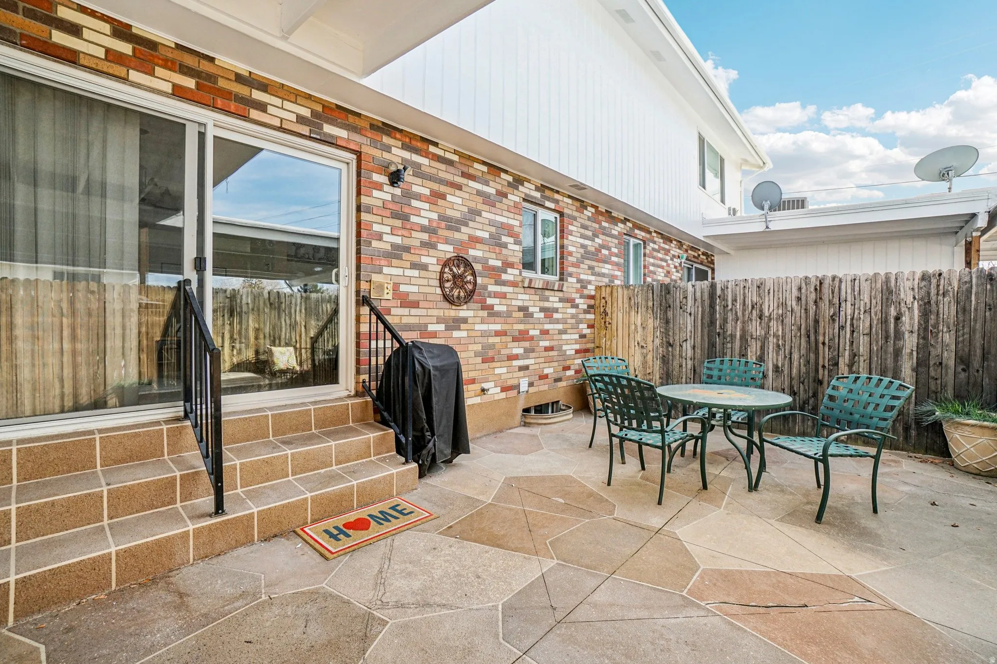 Outdoor patio featuring multi-toned flagstone paving, a privacy fence, and brick exterior siding