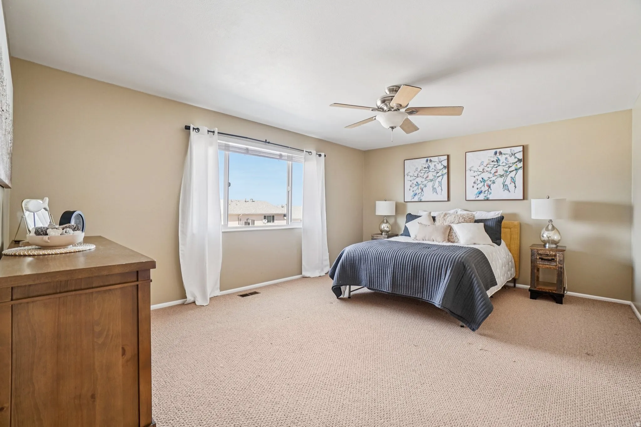 Spacious room featuring neutral wall tones, textured carpet flooring, a ceiling fan with light fixture, and a large window providing natural light