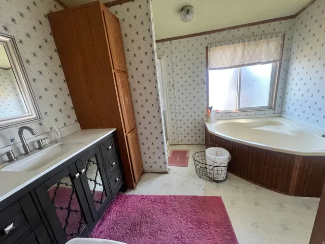 Spacious bathroom featuring a corner soaking tub, a single vanity with a white countertop and chrome faucet, and a tall wood-finish storage cabinet