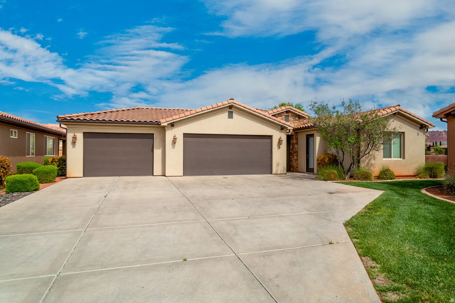 Stucco exterior property featuring a terracotta tile roof, two garage doors, a concrete driveway, and a manicured lawn