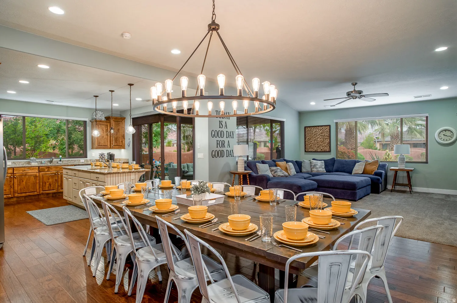 Open-concept interior featuring wood-finish flooring, a large dining area with a chandelier, a kitchen with wood cabinetry and an island, and a living area with a ceiling fan