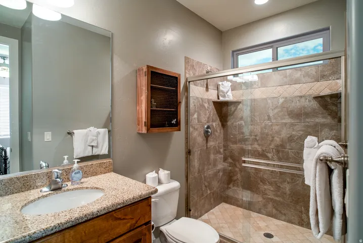 Tiled shower enclosure with a glass door, upper transom window, vanity with granite countertop, and wood-finish cabinetry