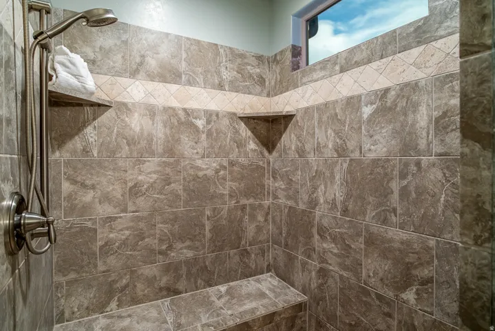 Shower enclosure featuring floor-to-ceiling stone-look tiling, a decorative tile accent band, and a brushed nickel shower fixture with a handheld sprayer