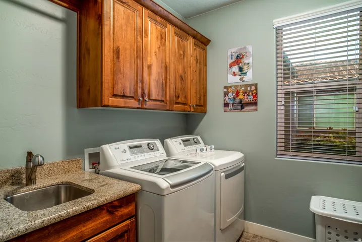 Dedicated laundry area featuring wood cabinetry, a utility sink with a stone-finish countertop, and a window with blinds