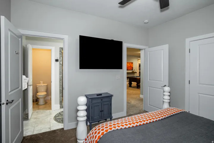 Bedroom with wall-mounted television, ceiling fan, and carpeted flooring