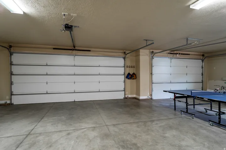 Spacious garage featuring two sectional garage doors with automatic openers, concrete flooring, and fluorescent overhead lighting