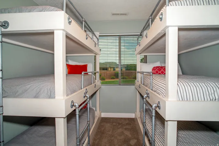Built-in bunk beds with industrial-style metal railings, soft gray wall paint, and a window with horizontal blinds