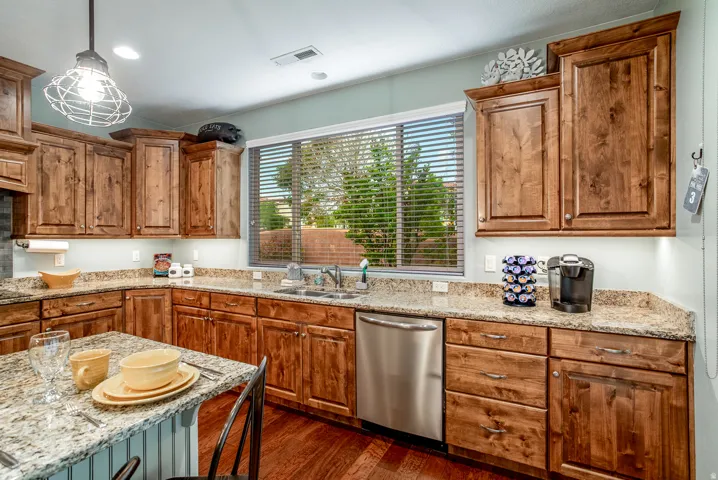 Kitchen featuring wood cabinetry, granite countertops, an undermount sink, a stainless steel dishwasher, and wood-finish flooring