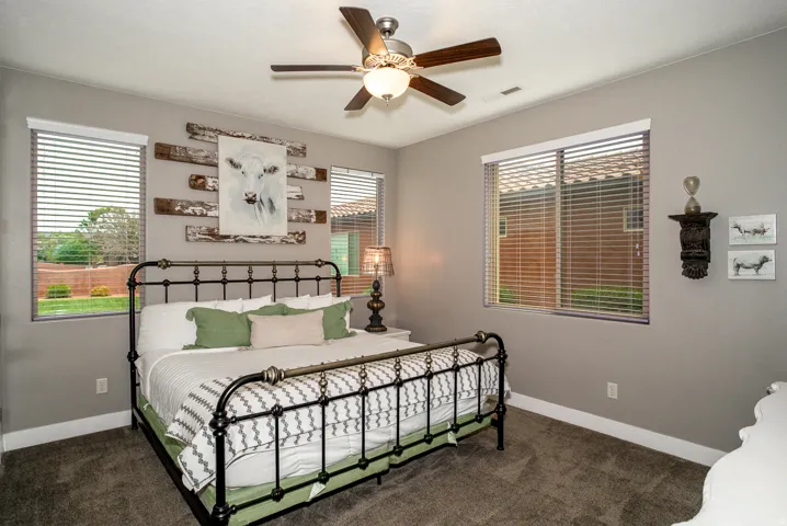 Spacious room featuring gray painted walls, window blinds, dark carpet flooring, and a ceiling fan with integrated lighting