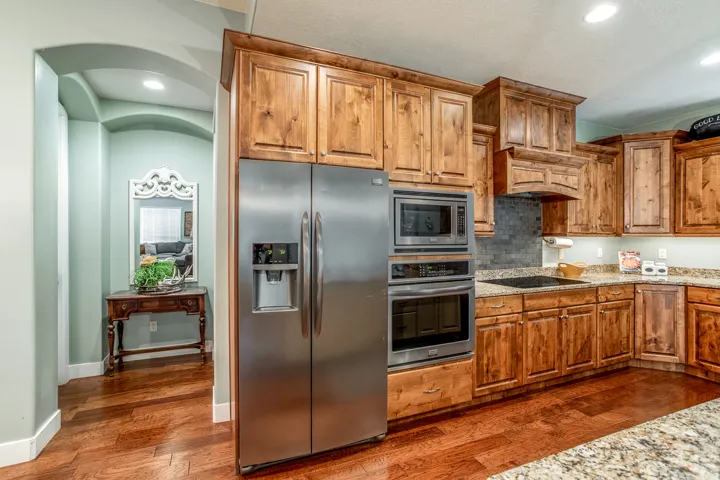 Kitchen featuring wood cabinetry, stainless steel appliances, a built-in microwave and oven, a cooktop, and stone countertops