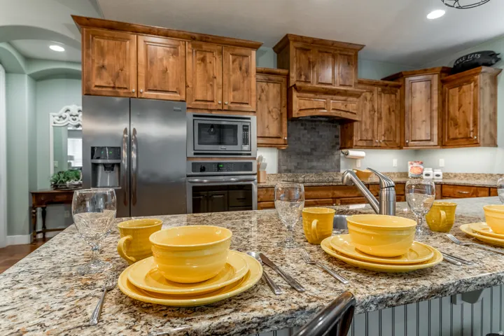 Kitchen featuring a spacious island with a speckled countertop, extensive wood cabinetry, stainless steel appliances including a refrigerator, microwave, and oven, and a tile backsplash