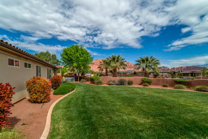Expansive rear yard featuring a manicured lawn, established landscaping, and a privacy wall