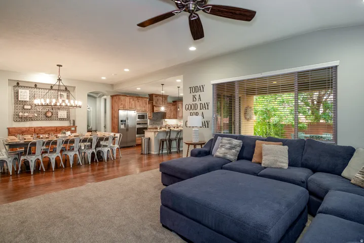 Open-concept living area featuring a broad sliding glass door, a ceiling fan with integrated lighting, recessed ceiling lights, wood-finish flooring, and a dining area with a linear chandelier