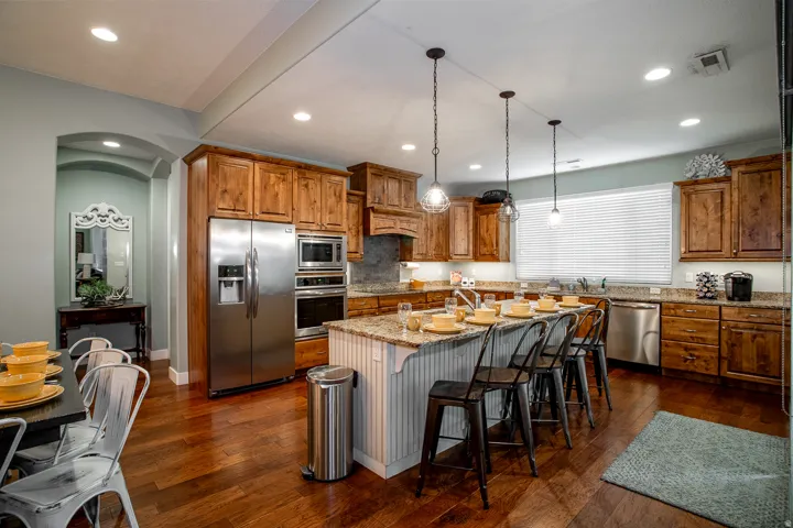 Spacious kitchen featuring stainless steel appliances, rich wood cabinetry, stone countertops, and a large island with pendant lighting