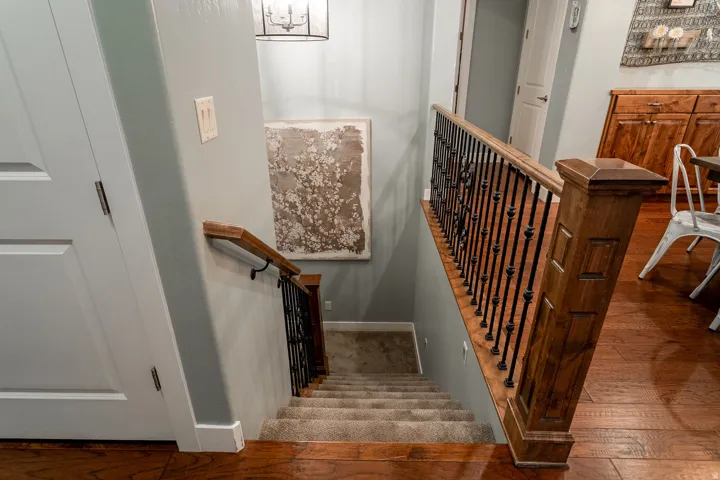 Staircase featuring wood-finish flooring, carpeted treads, wood newel post, wood handrails, and black metal balusters