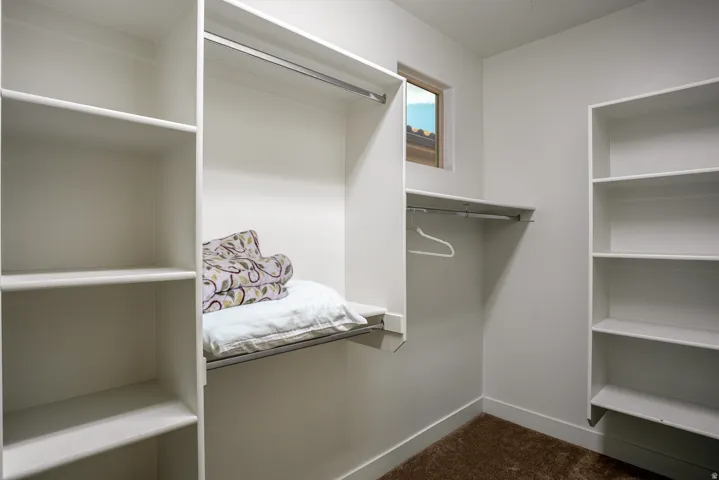 Walk-in closet featuring built-in shelving, hanging rods, light-toned walls, and a small window