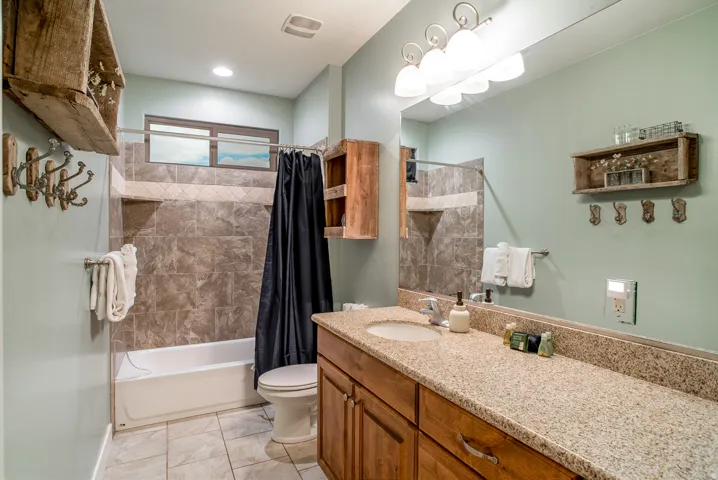 Full bathroom featuring a single vanity with a granite-style countertop, wood cabinetry, and a full-width mirror