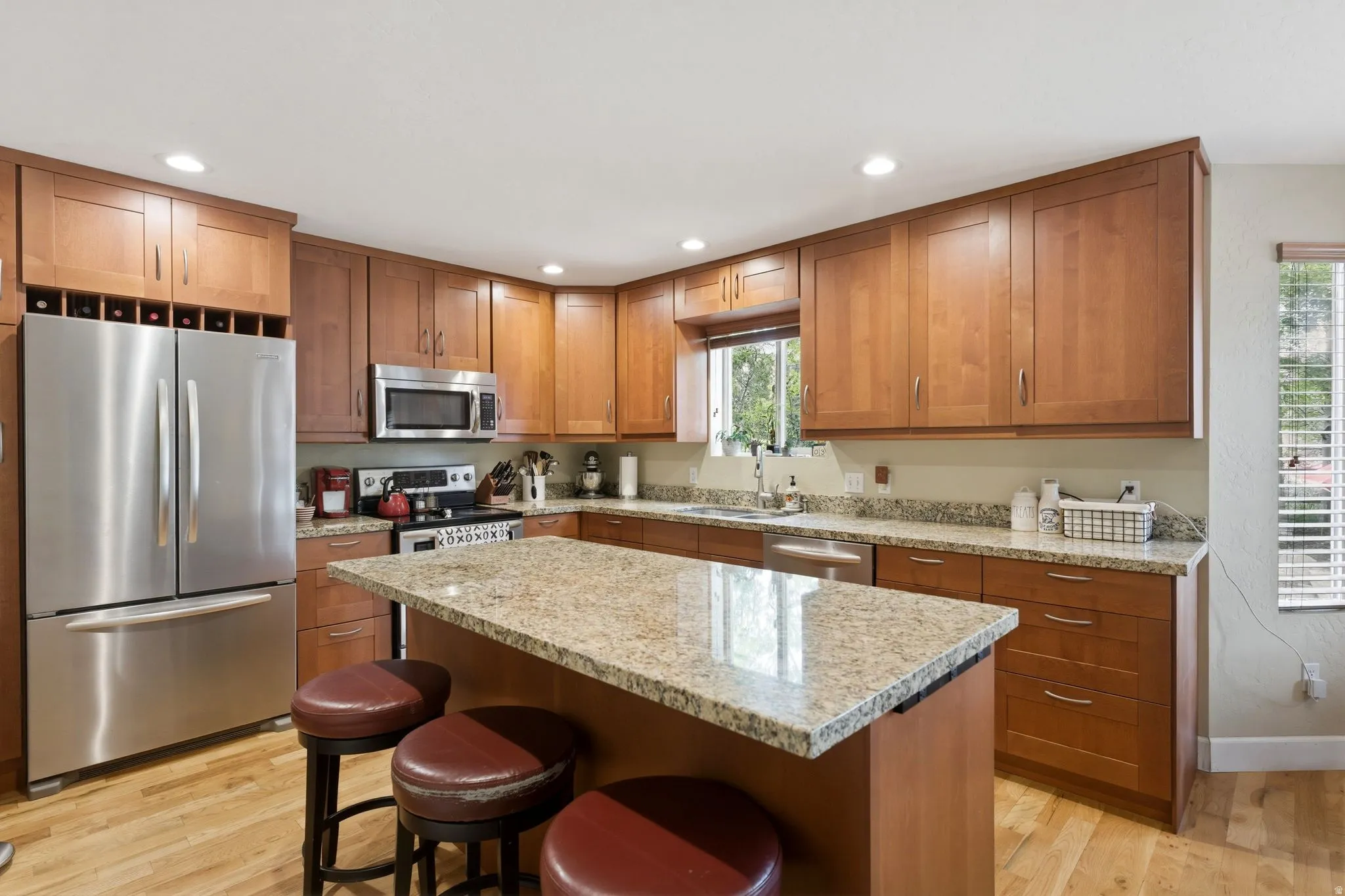 Kitchen featuring a large central island with a granite countertop, wood-finish flooring, recessed lighting, stainless steel appliances, and ample cabinetry with a built-in wine rack