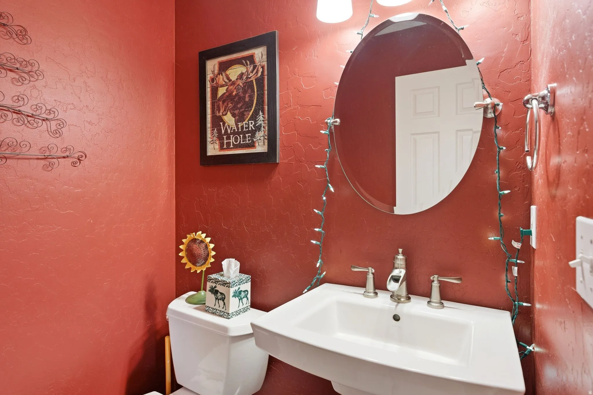 Pedestal sink with brushed nickel faucet, an oval mirror, and red textured walls