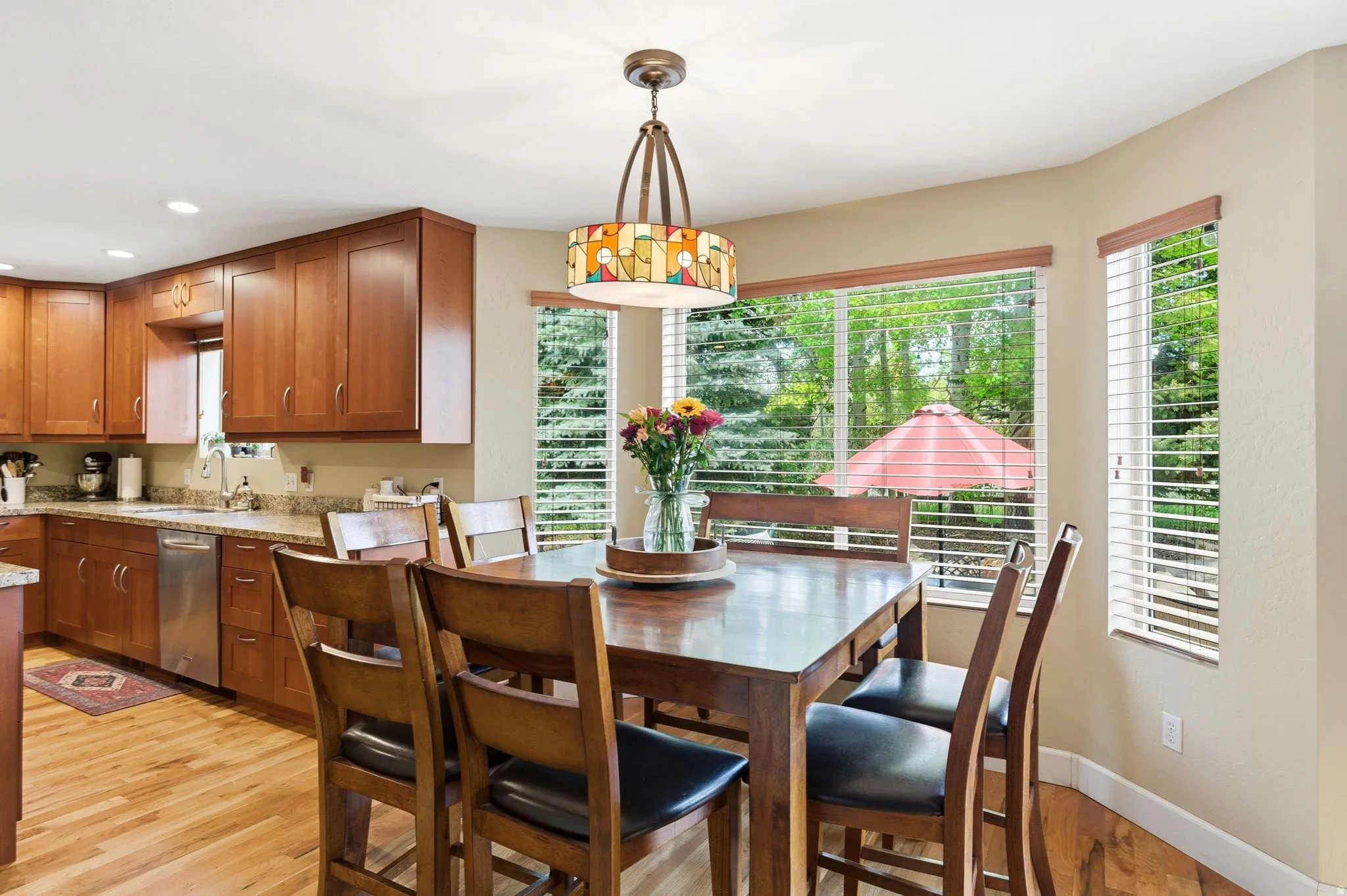 Dining area featuring a decorative pendant light fixture, wood-finish flooring, and multiple windows with horizontal blinds