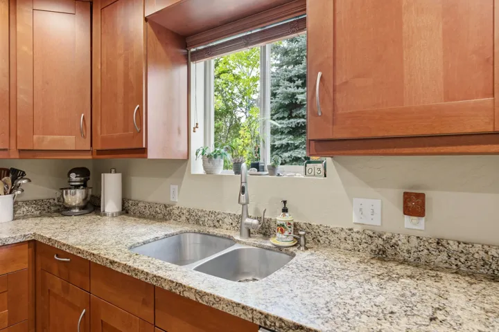 Kitchen featuring a double stainless steel sink, granite countertops, wood cabinetry, and a window with a green tree backdrop