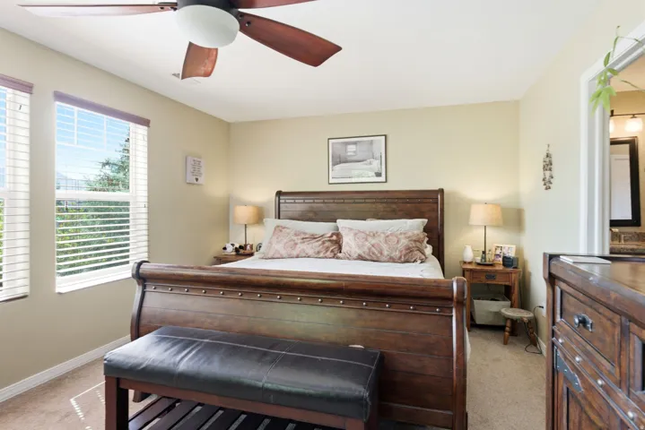 Bedroom featuring a ceiling fan with integrated lighting, two windows with blinds, and neutral tone wall paint
