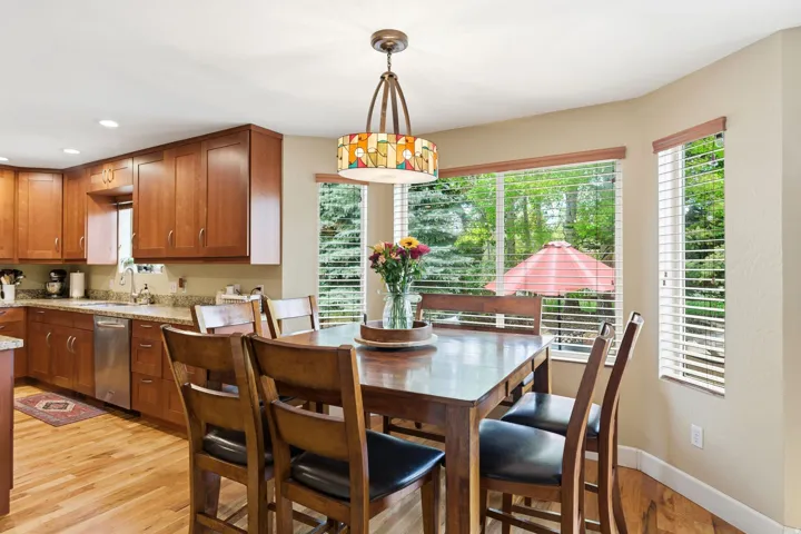 Dining area featuring a decorative pendant light fixture, wood-finish flooring, and multiple windows with horizontal blinds