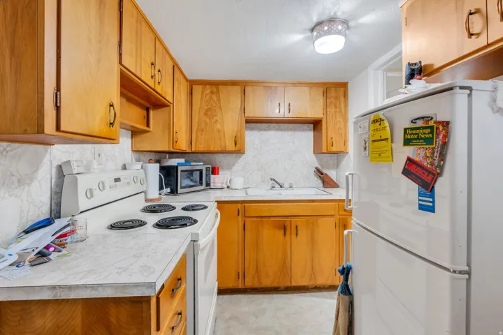 Functional kitchen featuring wood cabinetry, laminate countertops, a white electric range, a white refrigerator, and a recessed ceiling light fixture