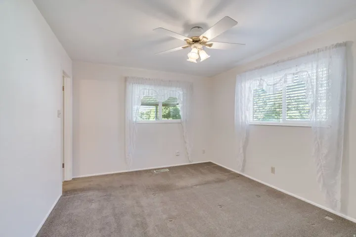 Room featuring dual windows with blinds, neutral wall paint, ceiling fan with light fixture, and carpet flooring