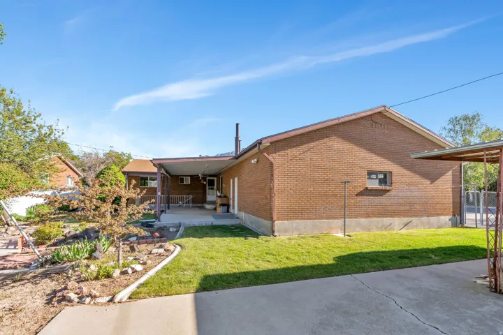 Brick exterior with a covered patio, concrete patio, and a grass lawn