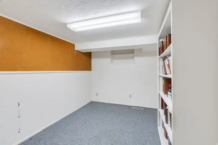 Room featuring built-in shelving, gray carpet flooring, white walls with wainscoting, and a cork board accent wall
