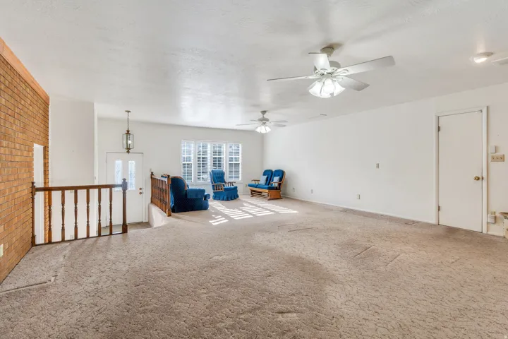 Spacious living area featuring a brick accent wall, white painted walls, and ample natural light from multiple windows