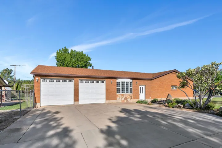 Brick exterior featuring a two-car garage with white paneled doors, an expansive concrete driveway, and a bay window with stone detailing
