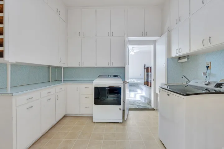 Dedicated utility room featuring extensive white cabinetry, light blue speckled countertops, tile flooring, and a built-in utility sink