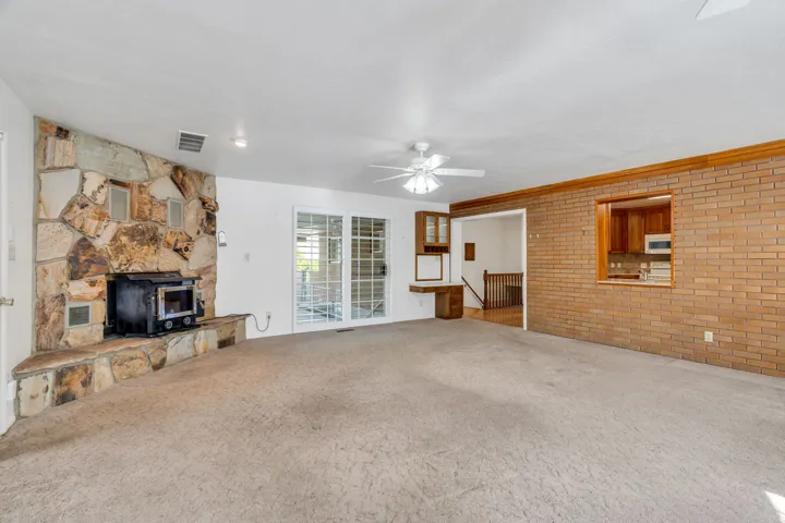 Spacious living area featuring a prominent stone fireplace with a wood-burning stove, light-colored carpeting, and white walls